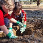 two little girls planting a tree, together